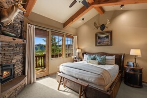 Un dormitorio con chimenea de piedra, una cama grande, un banco y vistas al exterior.