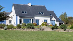 Une maison à deux étages, dotée d’un mur de soutènement en pierre, d’un toit en pente et d’une pelouse bien entretenue.