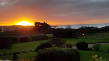 A sunset over a residential area with a view of the sea, a grassy lawn, and a stone wall.