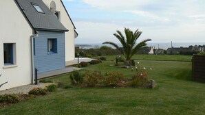 Une maison avec un toit en pente, une antenne parabolique et une pelouse bien entretenue, agrémentée d’un palmier et de fleurs.