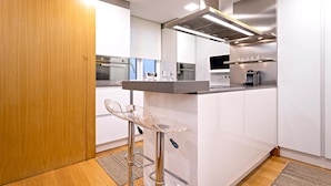 A modern kitchen with white cabinetry, stainless steel appliances, and a clear glass bar stool. - Exclusive Apartament in the Center. Tetuán III (Seville)