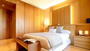 A modern hotel room with a large bed, wooden panel walls, a bedside table with lamps, and a small wooden bench. - Exclusive Apartament in the Center. Tetuán III (Seville)