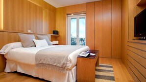 A modern bedroom with wooden paneling, a large bed with white linens, a bedside table with a magazine, and a TV on the right. - Exclusive Apartament in the Center. Tetuán III (Seville)
