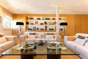 Una sala de estar moderna con una mesa de centro de vidrio, sofás blancos y una estantería de madera con libros y objetos decorativos.