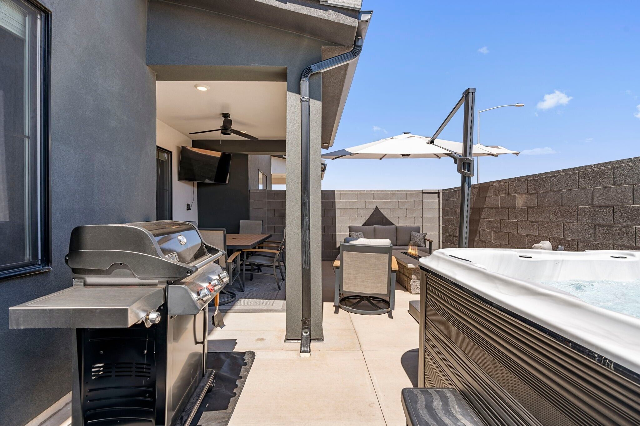 An outdoor patio with a grill, seating area, and hot tub.