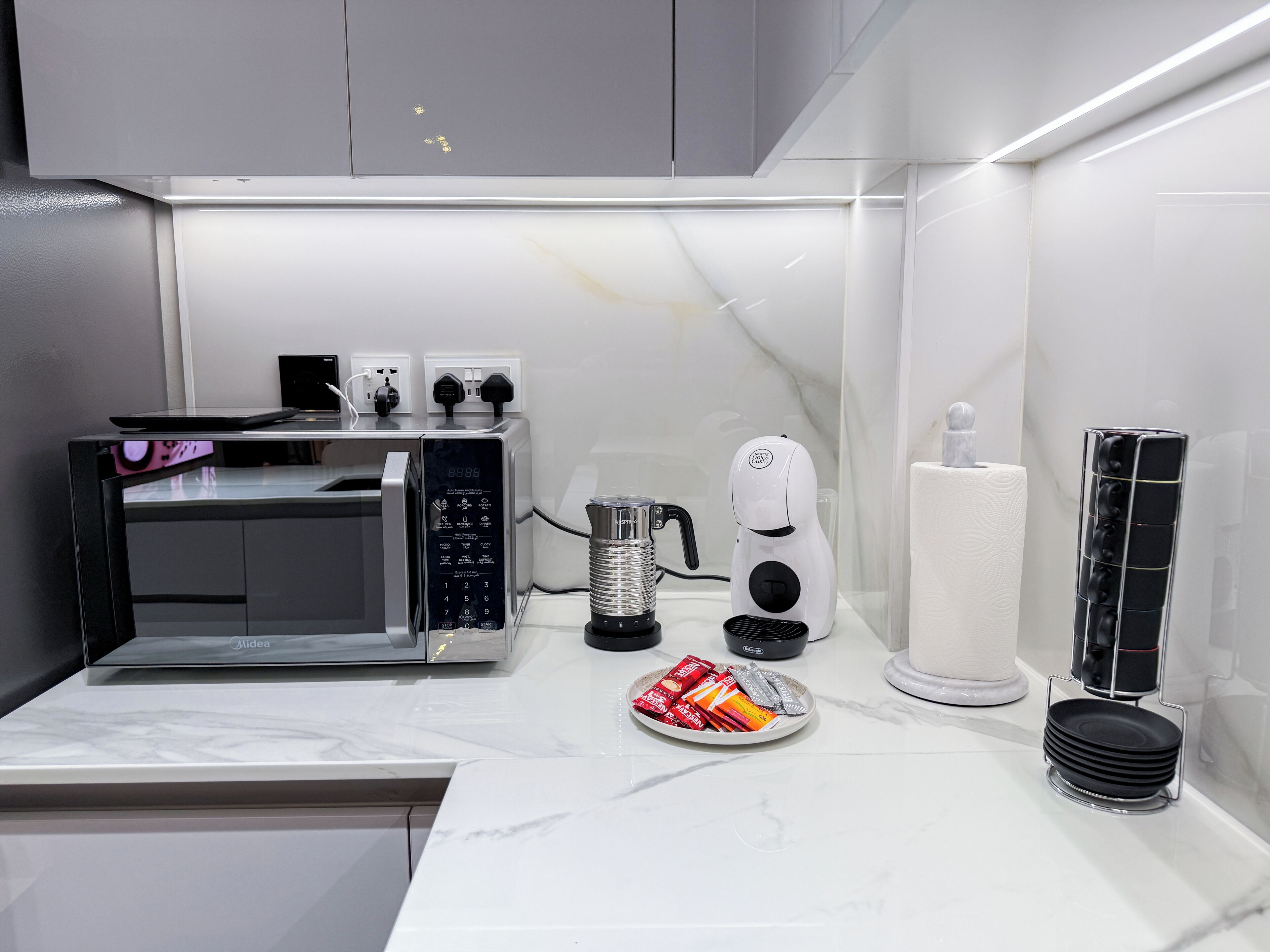A modern kitchen with a microwave, toaster, kettle, and a plate of snacks.