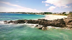 Paesaggio costiero con acque cristalline turchesi, spiaggia sabbiosa e affioramenti rocciosi.