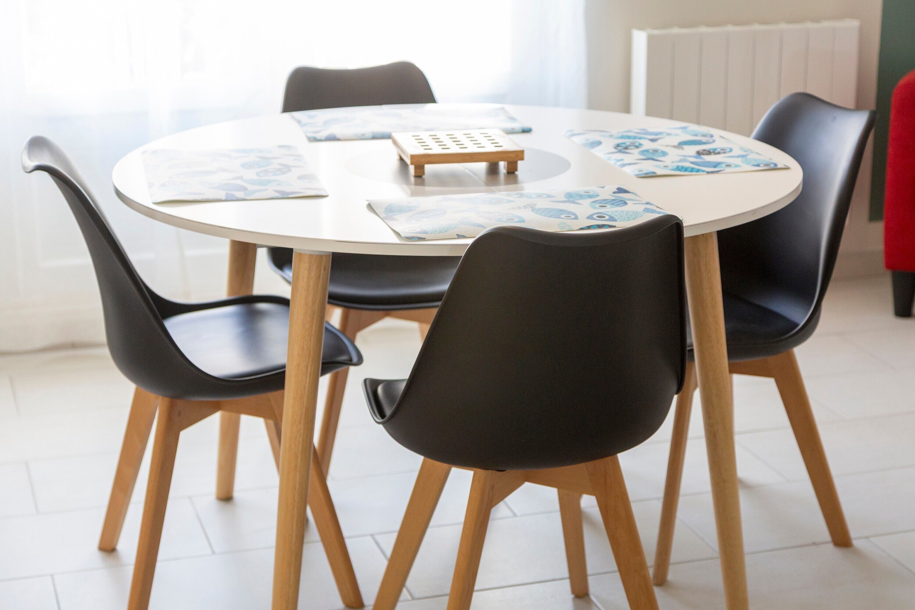 Een ronde eettafel met vier stoelen, een klein houten blokje en een placemat met een blauw patroon.