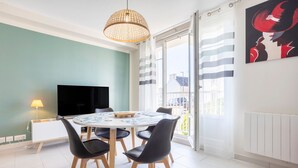 Zona pranzo con tavolo rotondo, sedie nere, televisione a schermo piatto e lampadario a sospensione.