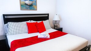 A neatly made bed with a red throw, a white pillow, and a checkered pillow. - Hostel Horizon  (Kissimmee)