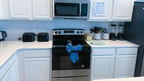 A kitchen with white cabinets, a microwave, a stove, a toaster, and a blender. - Hostel Horizon  (Kissimmee)