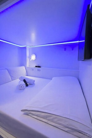 A modern hotel room with a large bed, a bedside table, a wall-mounted lamp, and a flat-screen TV. - Modular Dreams Hostel (Madrid)