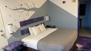 A hotel room with a bed, a nightstand, a wall-mounted phone, and a door leading to another room. - Special boutique hotel in Oxford, Alabama with a variety of themed rooms! (Oxford)