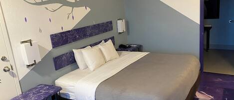 A hotel room with a bed, a nightstand, a wall-mounted phone, and a door leading to another room.