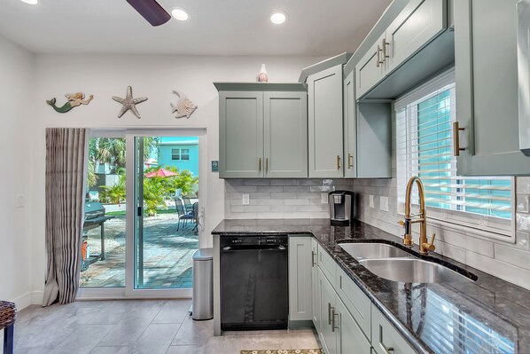 A modern kitchen with light green cabinets, a black dishwasher, and a stainless steel sink.