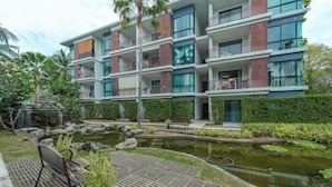 Een hotel met meerdere verdiepingen, balkons, een aangelegde tuin en een klein vijver.
