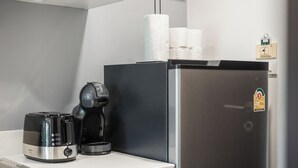 Een kitchenette met een zwarte koffiezetapparaat, een broodrooster en een roestvrijstalen koelkast.