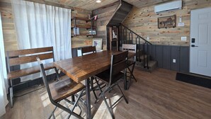 Ein rustikaler Innenraum mit einem Holzespeisetisch, Bänken, einer Treppe und einem an der Wand befestigten Regal mit verschiedenen Gegenständen.