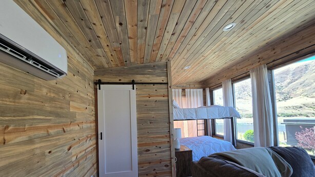 Ein Holzblockbau mit Bett, Fenster mit Seeblick und einer Schiebetür.
