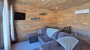 Ein gemütliches Blockhauskamin-Interieur mit Holzbalkendecke, Ecksofa, Wand-Fernseher und einer kleinen Treppe.