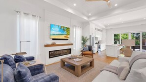 A spacious living room with a fireplace, a television mounted on the wall, and a large window offering a view of the outdoors. - Beach Days, Sunset Skies & Poolside Living (Naples)