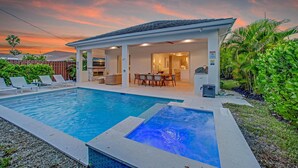 A modern house with a swimming pool, a patio with lounge chairs, and a covered outdoor area with a table and chairs. - Beach Days, Sunset Skies & Poolside Living (Naples)