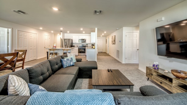 A modern living room with a sectional sofa, a coffee table, and a TV on the wall.