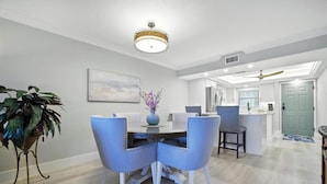 A dining area with a round table, blue striped chairs, a vase with flowers, and a ceiling light fixture. - 🌺Sand Pointe 214- All New Luxury with Sweeping Gulf Views *POOL NOT OPEN🐬 (Sanibel)