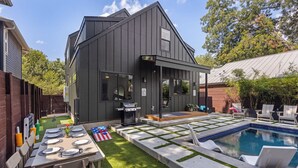 A modern house with a pool, a barbecue area, and a dining setup with outdoor furniture.