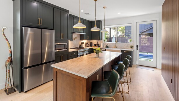 A modern kitchen with dark cabinets, stainless steel appliances, pendant lighting, and a central island with bar stools.