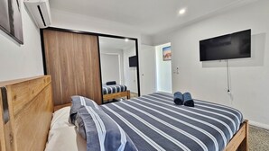 Un dormitorio con una cama, cabecera de madera, televisor montado en la pared y un espejo.