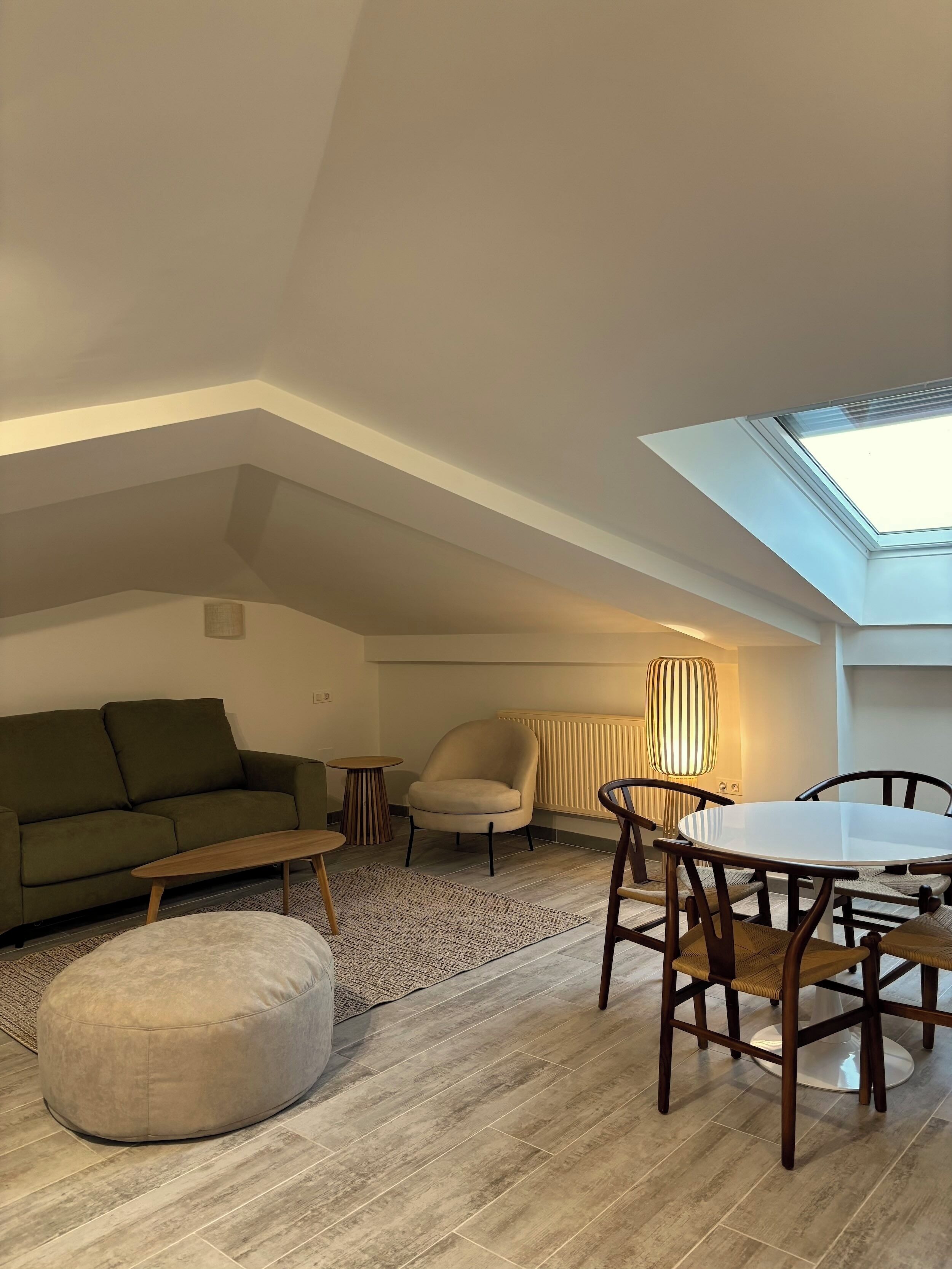 Een modern loft appartement met dakraam, een groene bank, een ronde eettafel en een beige fauteuil.