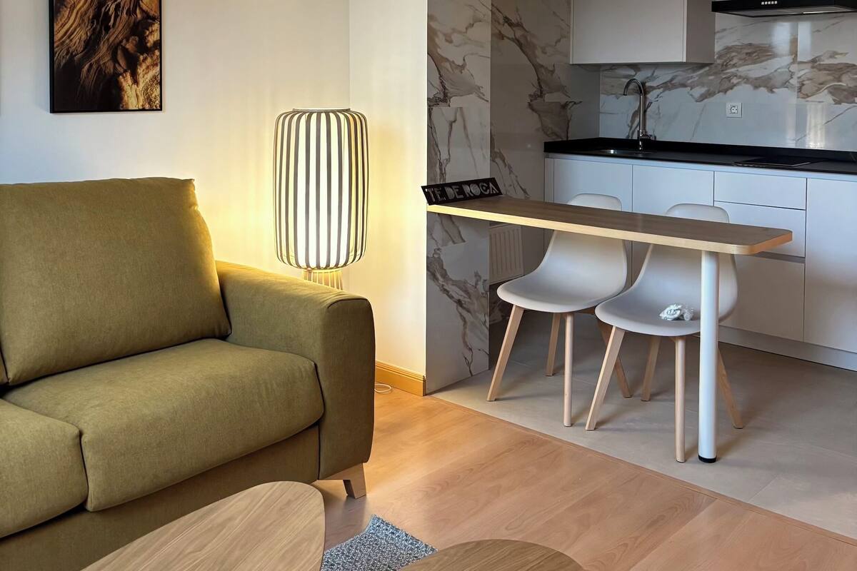 A modern living room with a sofa, a coffee table, and a dining area with a table and chairs.