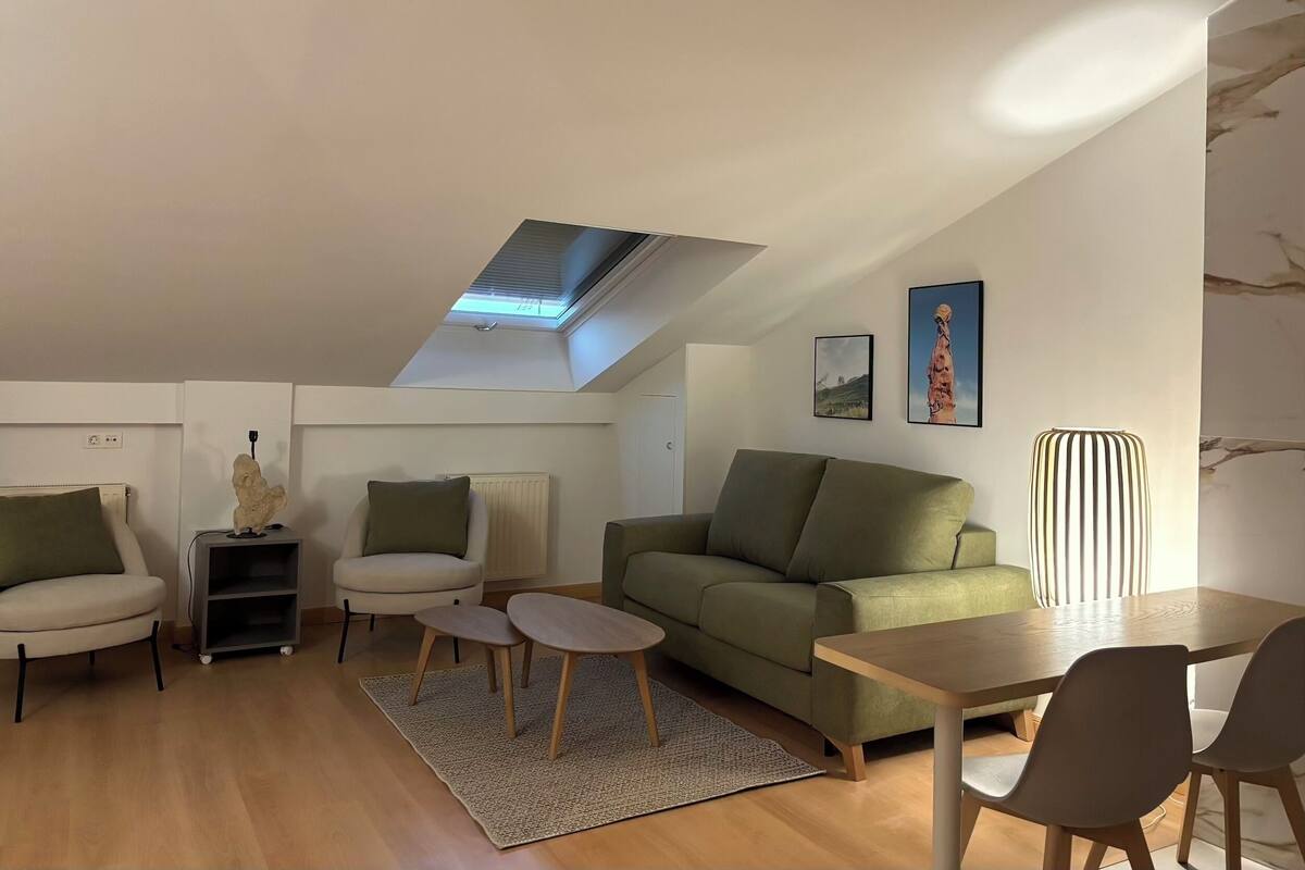 A modern living room with a skylight, a green sofa, a wooden coffee table, and a dining area with chairs.