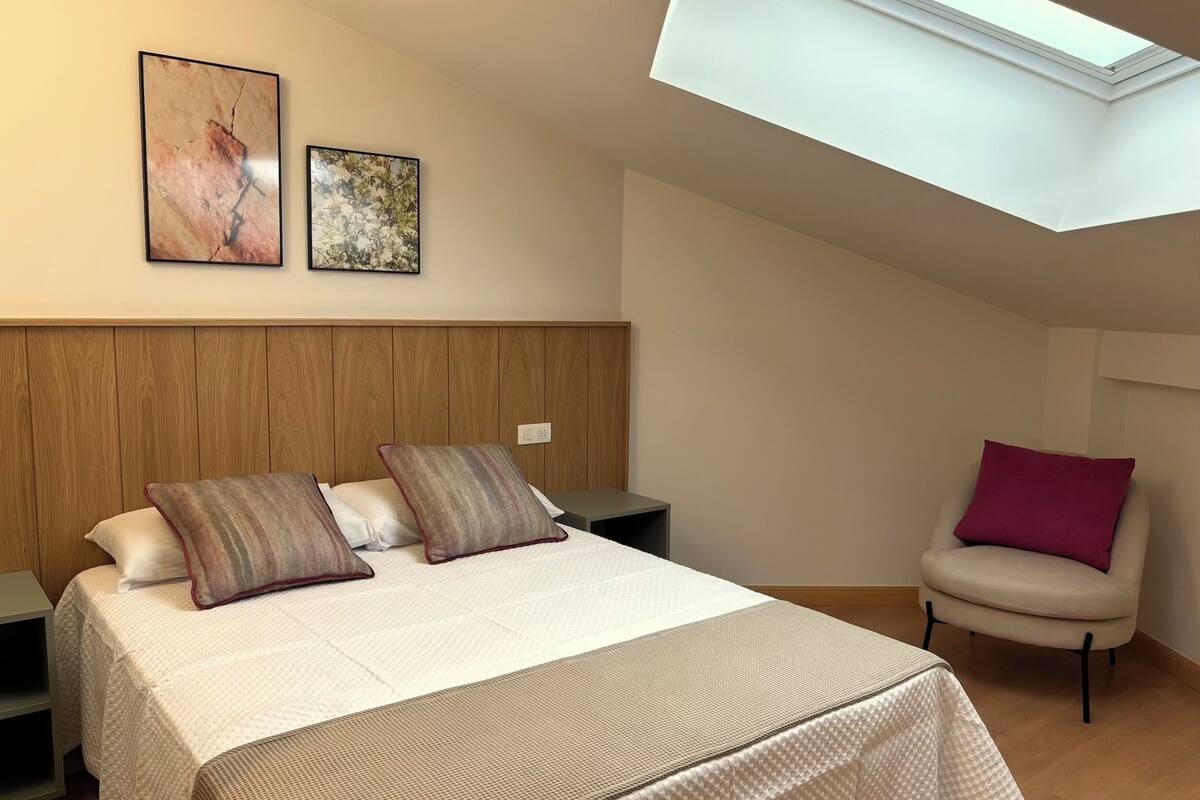 A bedroom with a bed, a chair, a nightstand, and a skylight.