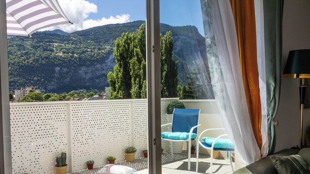 A balcony with a view of mountains, a white chair, a blue chair, and a sofa. - Cozy, Spacious condo with balcony and beautiful serene mountain views. (Cluses)