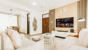 Een moderne woonkamer met een zithoek, een salontafel, een aan de muur bevestigde televisie en een plafondventilator.