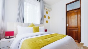 Een keurig opgemaakt hotelkamer met een bed, nachtkastje, lamp en een deur.