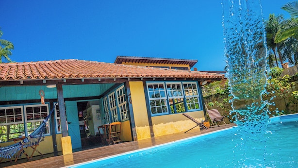 A pool area with a tiled roof, a hammock, and a water fountain. - Pousada Casa do Pescador Camburi (São Sebastião)