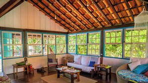 A spacious room with a high ceiling, large windows, a sofa, a chair, and a small table. - Pousada Casa do Pescador Camburi (São Sebastião)