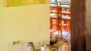 A room with a painting on the wall, a wooden table with decorative vases, and a view of the outside through a window. - Pousada Casa do Pescador Camburi (São Sebastião)