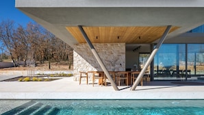 A modern outdoor pool area with stone walls, wooden furniture, and a clear view of the surrounding landscape. - Villa bOX by Villas Guide (Brajkovici)