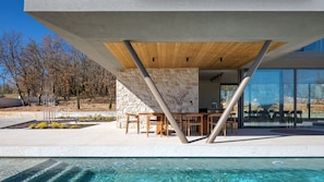 A modern outdoor pool area with stone walls, wooden furniture, and a clear view of the surrounding landscape.