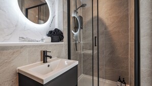Ein modernes Badezimmer mit Marmorwaschtisch, einer Duschkabine aus Glas und einem großen Spiegel.