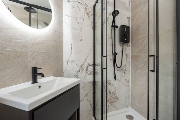 A modern bathroom with a white sink, a handheld showerhead, and a glass-enclosed shower area.