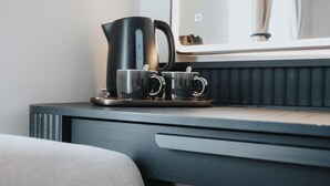 Une chambre d’hôtel moderne avec un bureau en bois foncé, une bouilloire électrique noire et deux tasses en acier inoxydable posées sur un plateau.