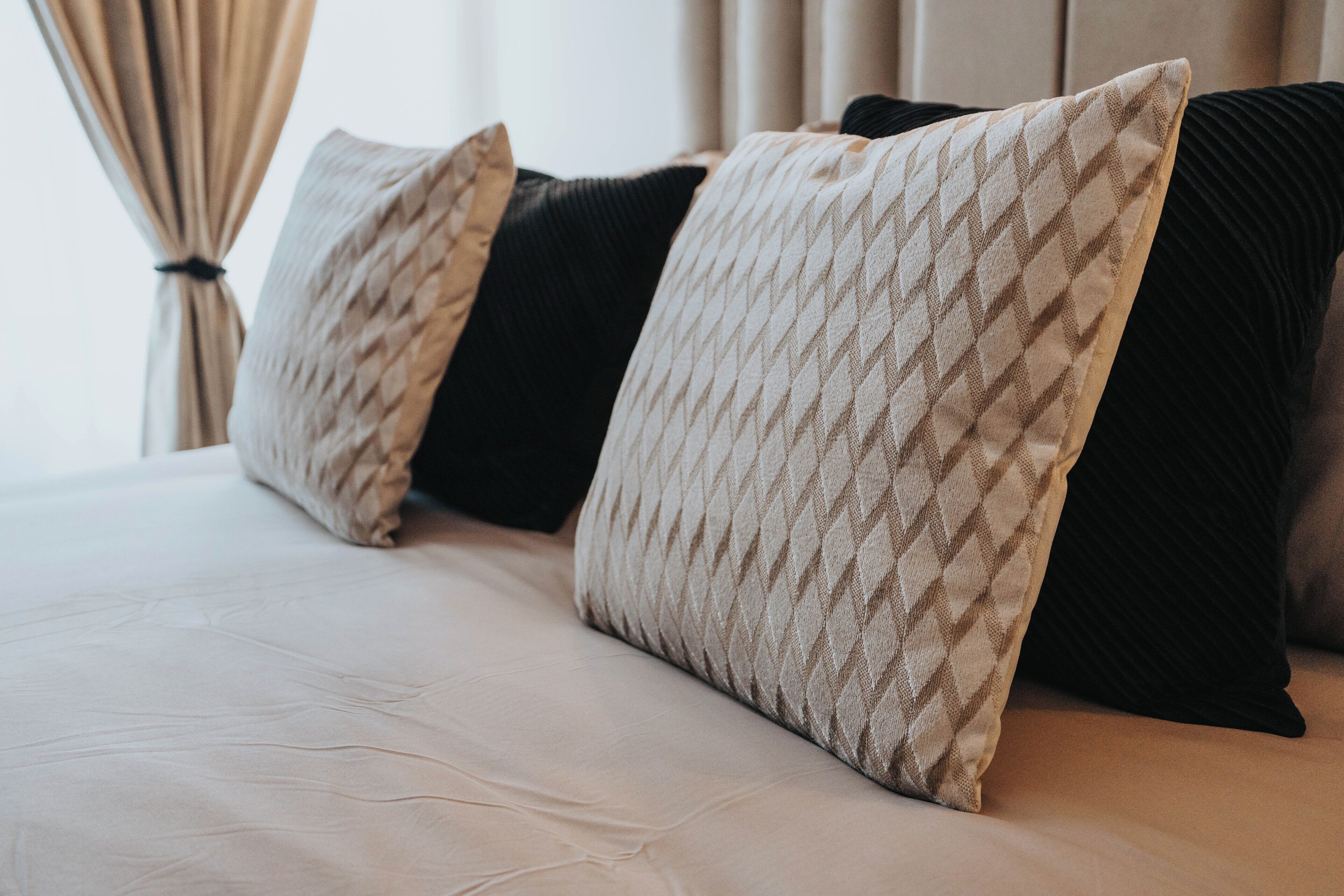 Ein Bett mit vielen Kissen, einer hellen Bettdecke und einem Vorhang im Hintergrund.