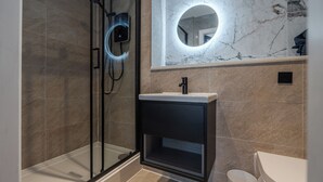A modern bathroom with a glass shower enclosure, a pedestal sink, and a marble-tiled wall with a circular mirror. - Bold St | King Room | Fireplace | Private Ensuite (Liverpool)
