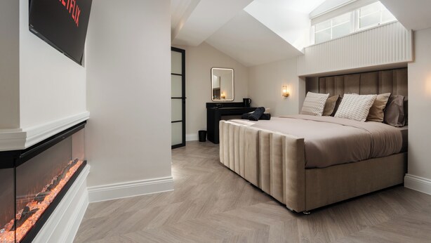 A modern bedroom with a bed, a TV mounted on the wall, a fireplace, and a skylight. - Bold St | Skylight Charm with Fireplace | King Bed (Liverpool)