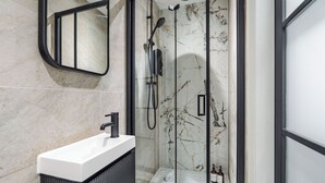 A modern bathroom with a glass-enclosed shower, a white sink, and marble walls. - Bold St | Skylight Charm with Fireplace | King Bed (Liverpool)